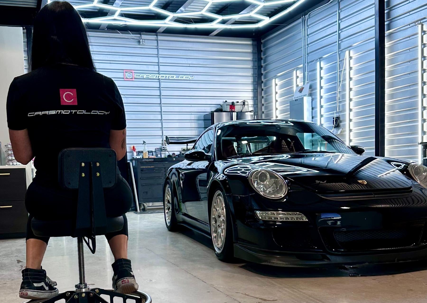 Person using a mobility scooter in a garage with a black Porsche car.